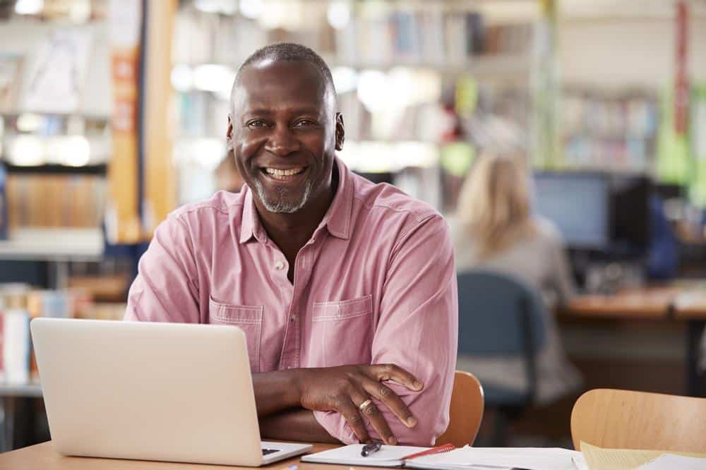 Black middle aged man smiling by his laptop